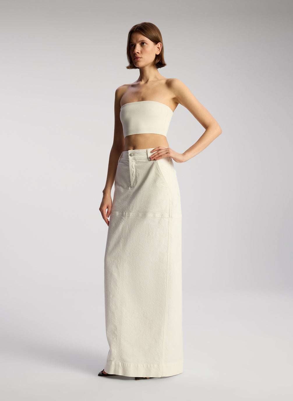 side view of woman wearing off white cropped strapless top with white maxi skirt