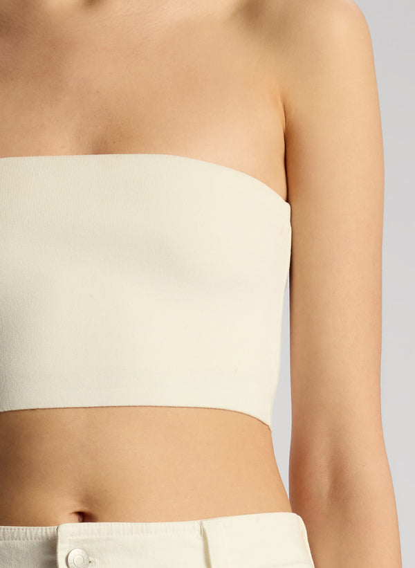 detail view of woman wearing off white cropped strapless top with white maxi skirt