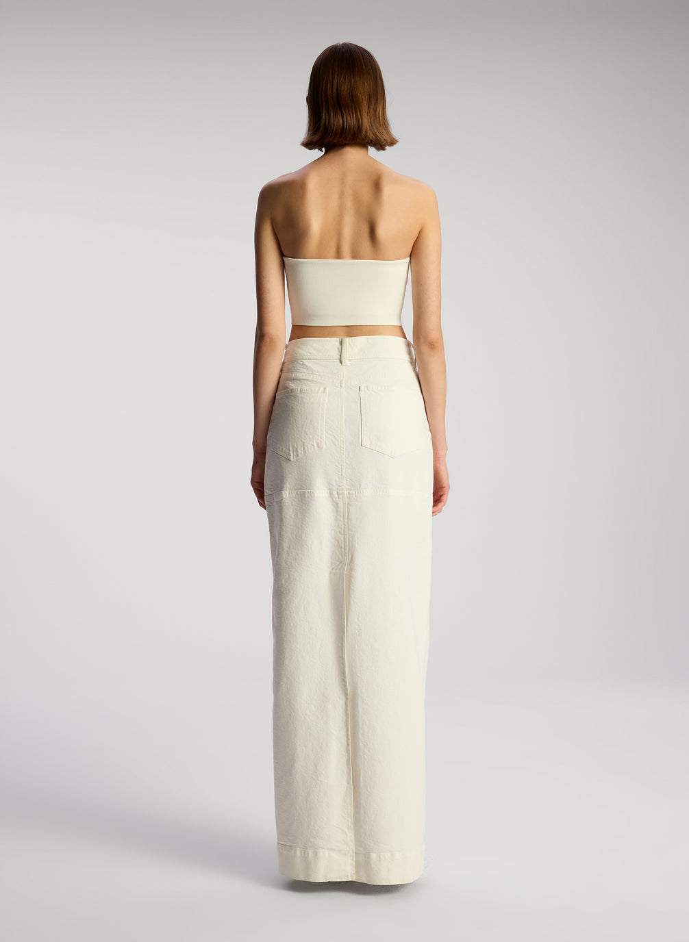 back view of woman wearing off white cropped strapless top with white maxi skirt