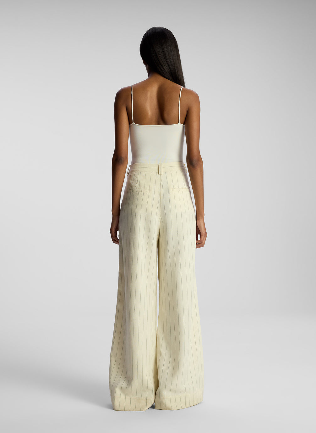 back view of woman earing cream bodysuit and cream pinstripe pant