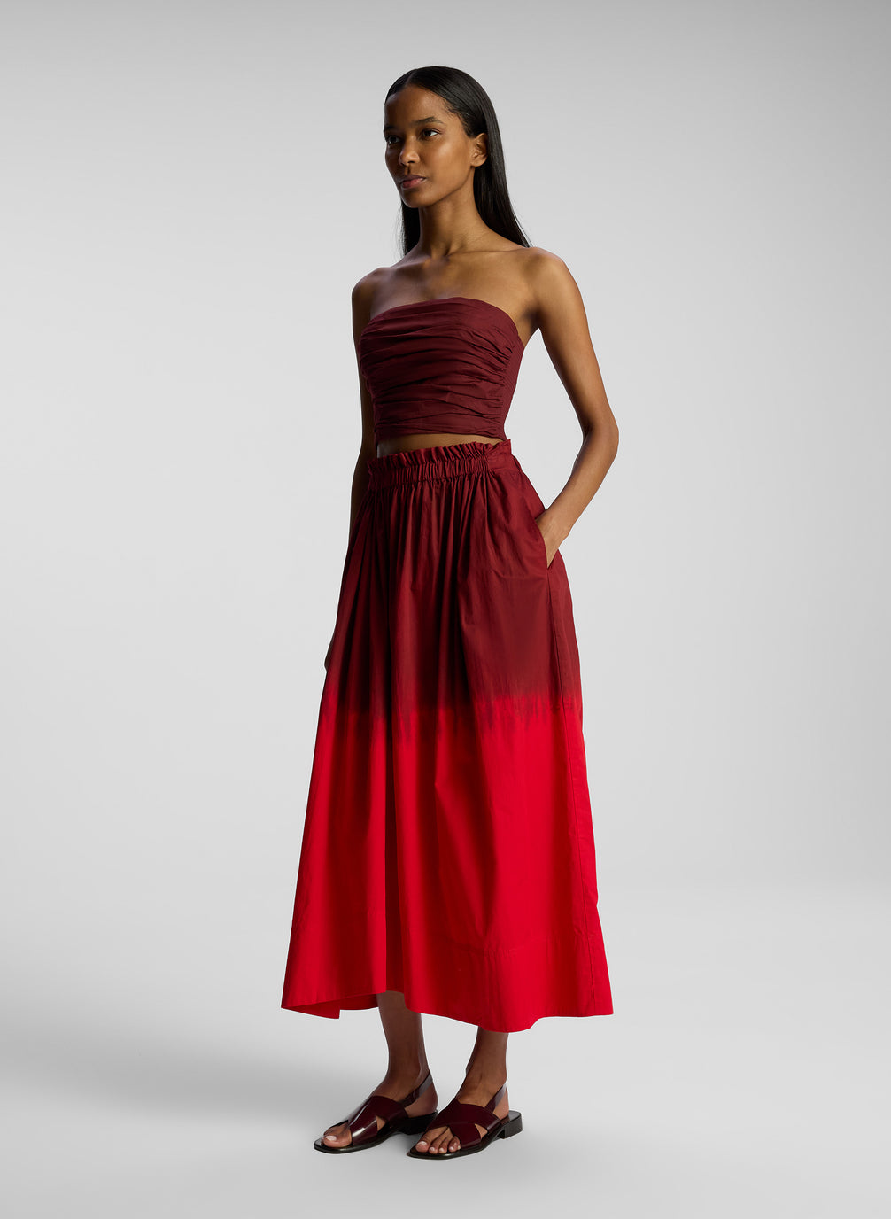 side view of woman wearing burgundy strapless top and matching midi skirt