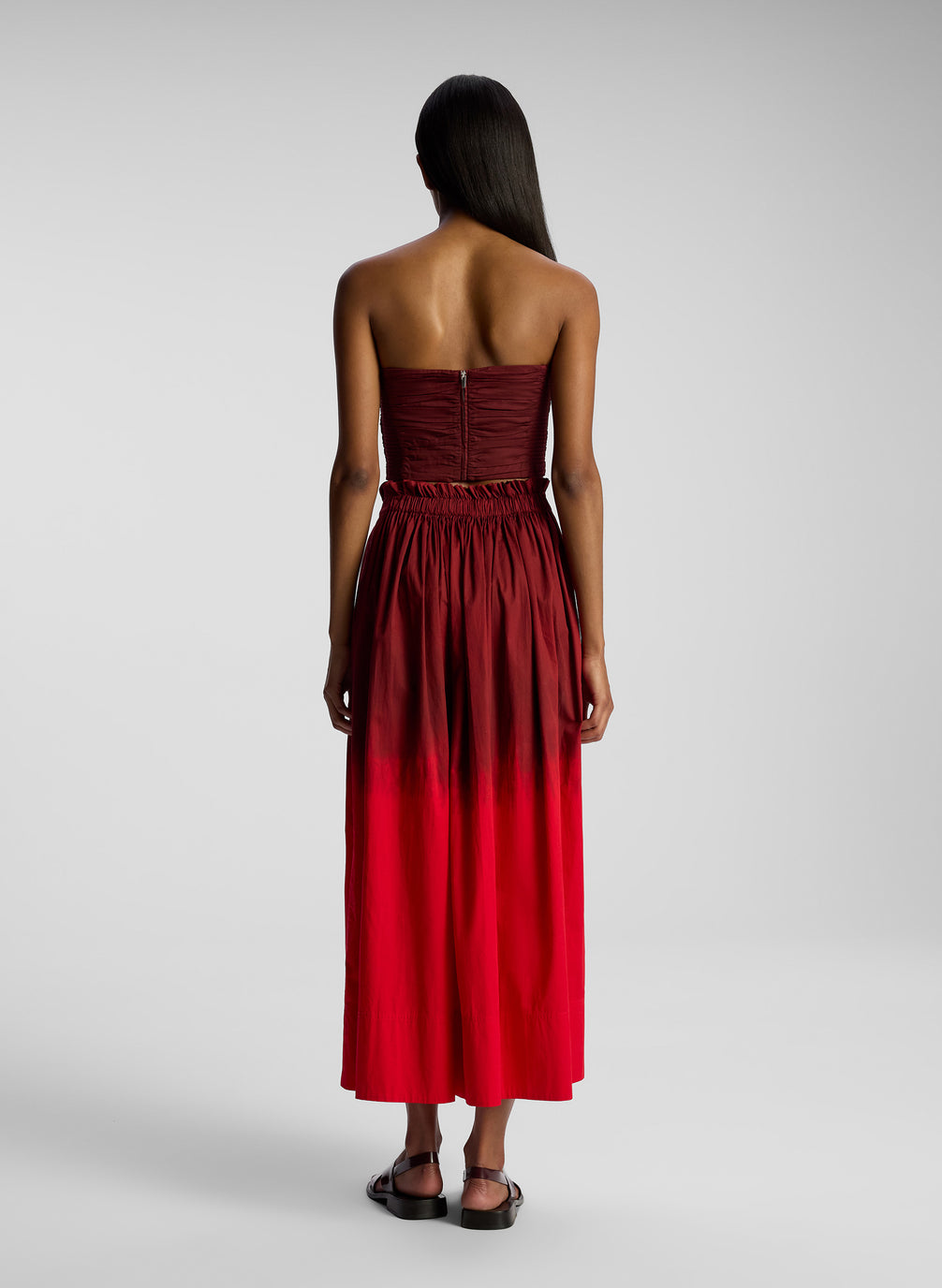 back view of woman wearing burgundy strapless top and matching midi skirt