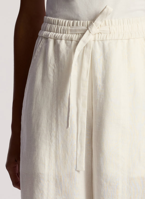 detail view of woman wearing white asymmetric tank top and cream linen wide leg pants