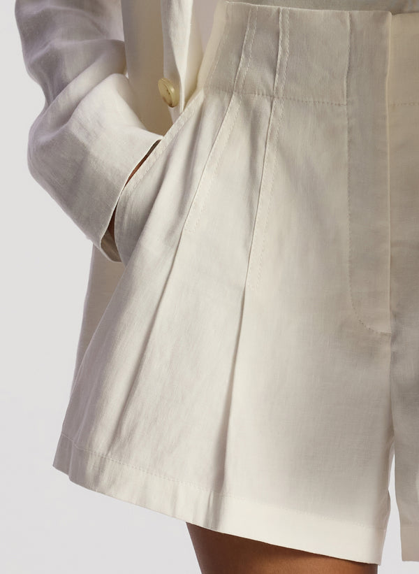 detail view of woman wearing a white blazer, a white tee shirt and ecru shorts