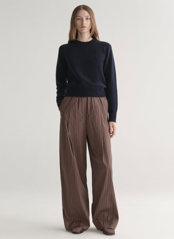 Person wearing a blue sweater and brown pleated pants on a white background
