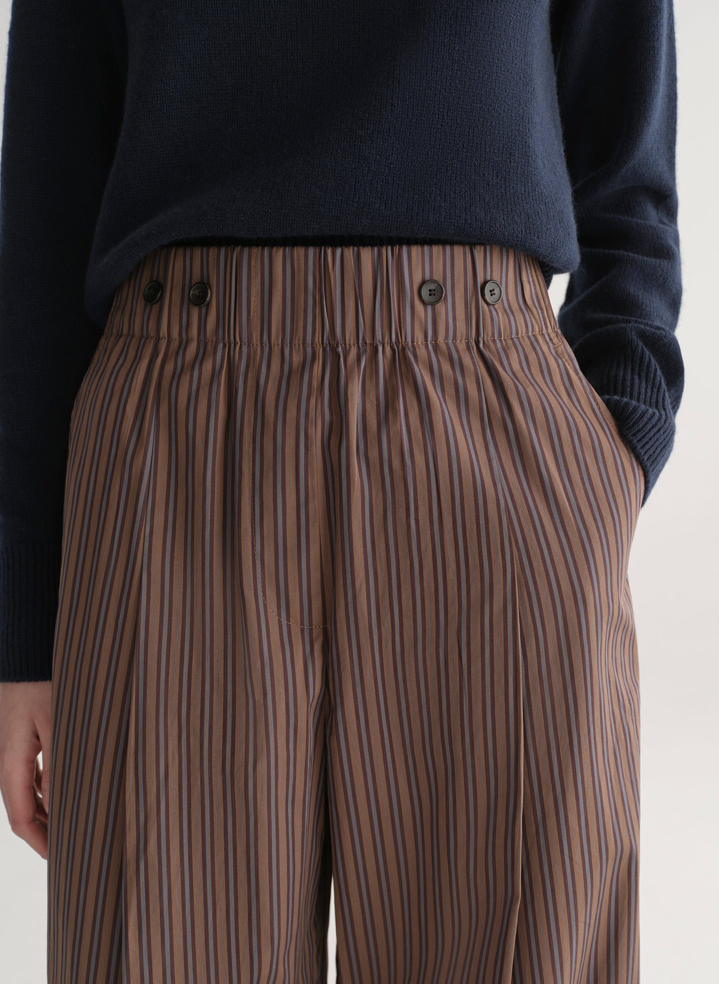 Brown striped pants worn with a dark sweater on a light background