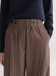 Brown striped pants worn with a dark sweater on a light background