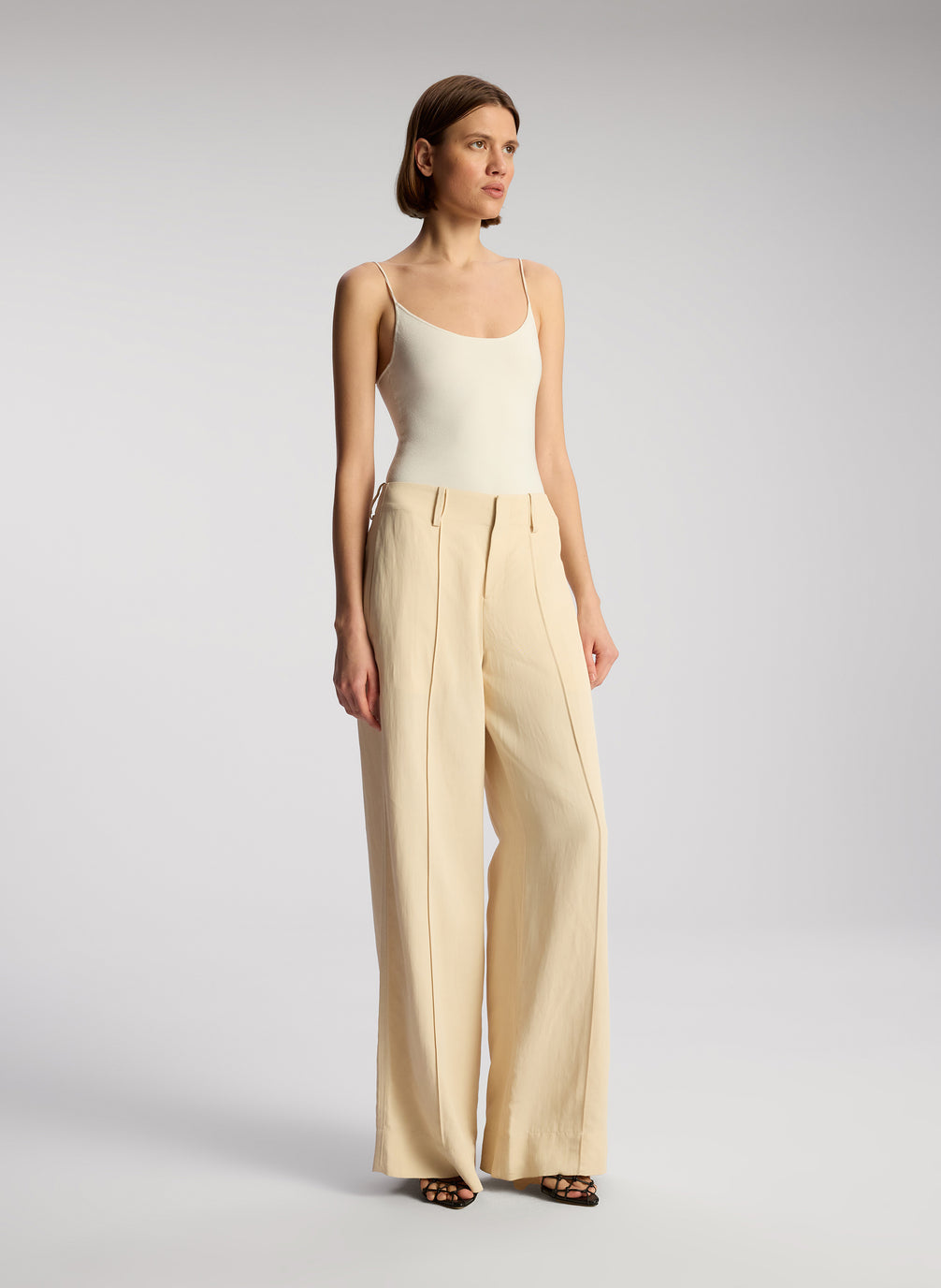 side view of woman wearing off white bodysuit and beige wide leg pants