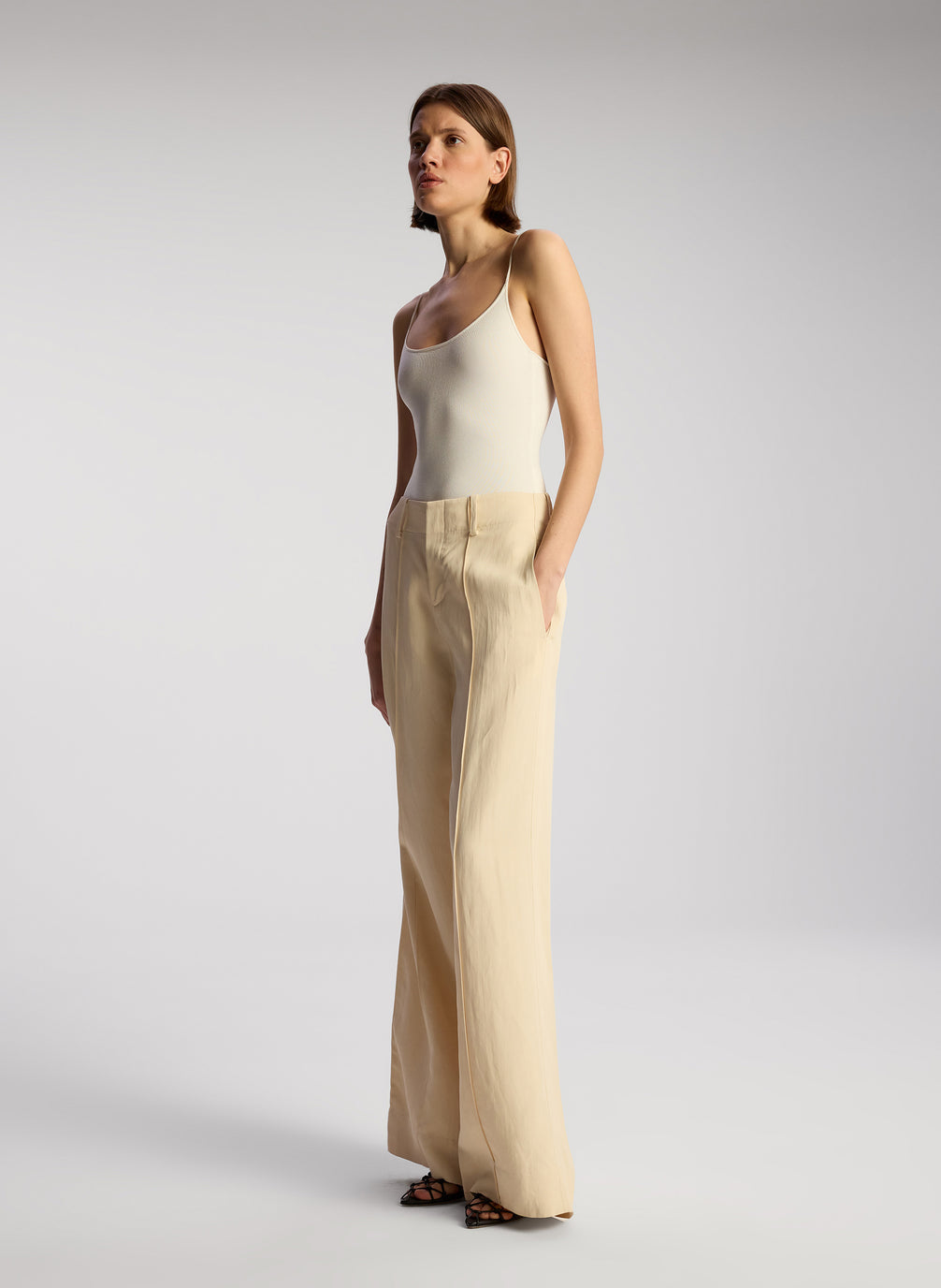 side view of woman wearing off white bodysuit and beige wide leg pants