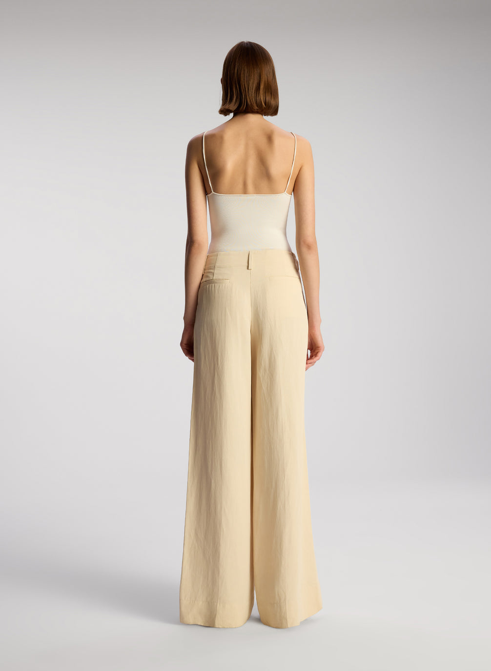 back view of woman wearing off white bodysuit and beige wide leg pants