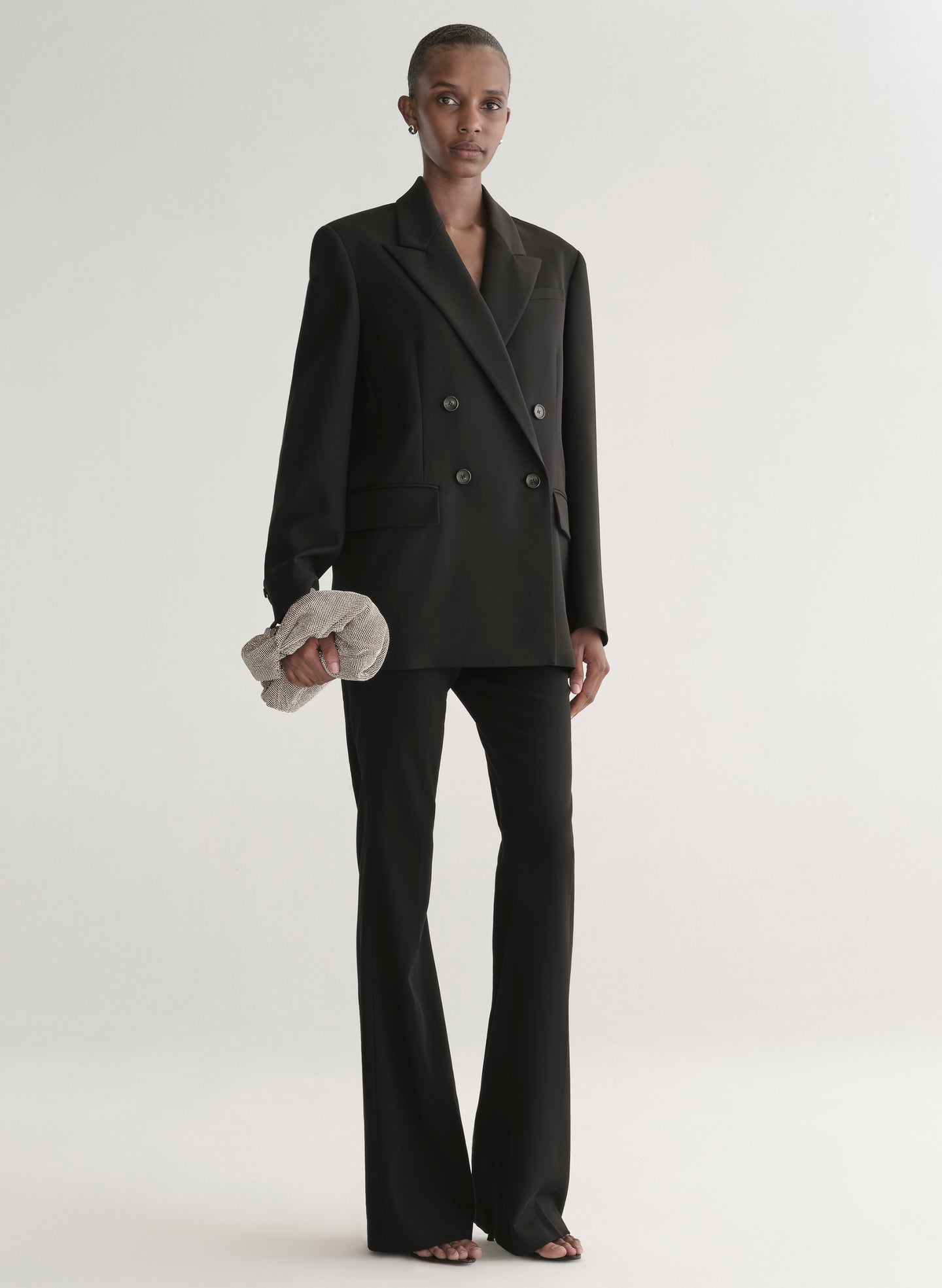 Person wearing a black suit holding a silver clutch against a light gray background