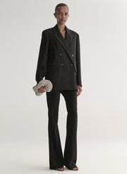 Person wearing a black suit holding a silver clutch against a light gray background