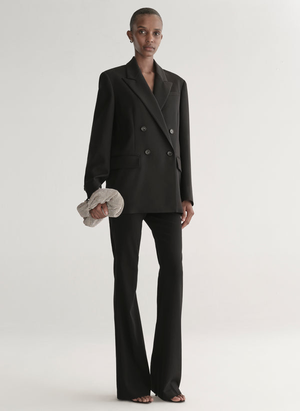 Person wearing a black suit holding a silver clutch against a light gray background