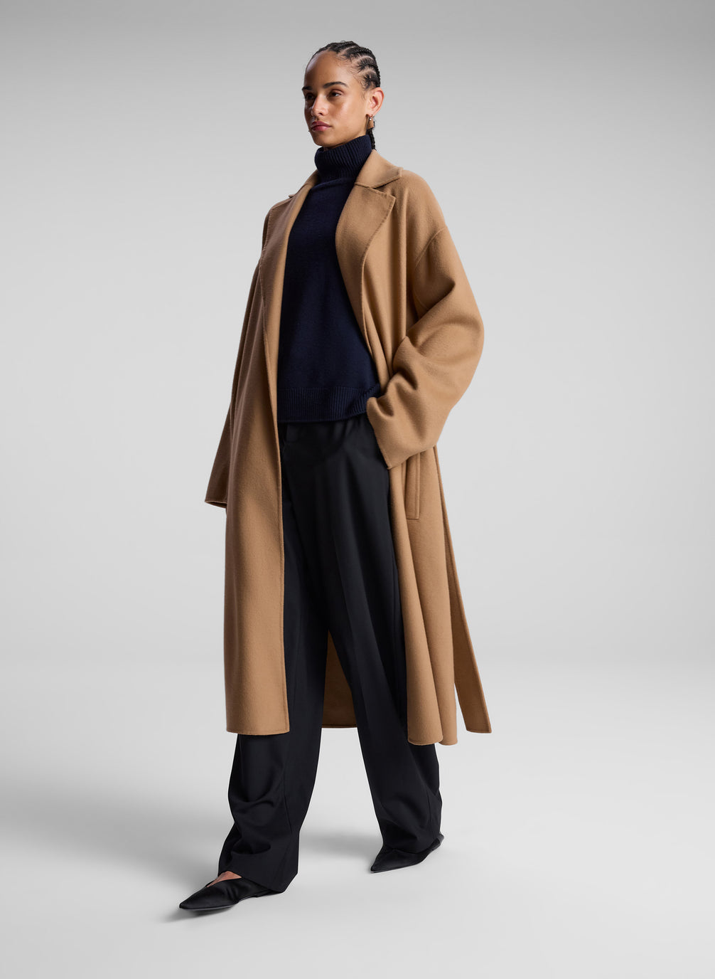 woman wearing camel color wool coat, black turtleneck, and black pants