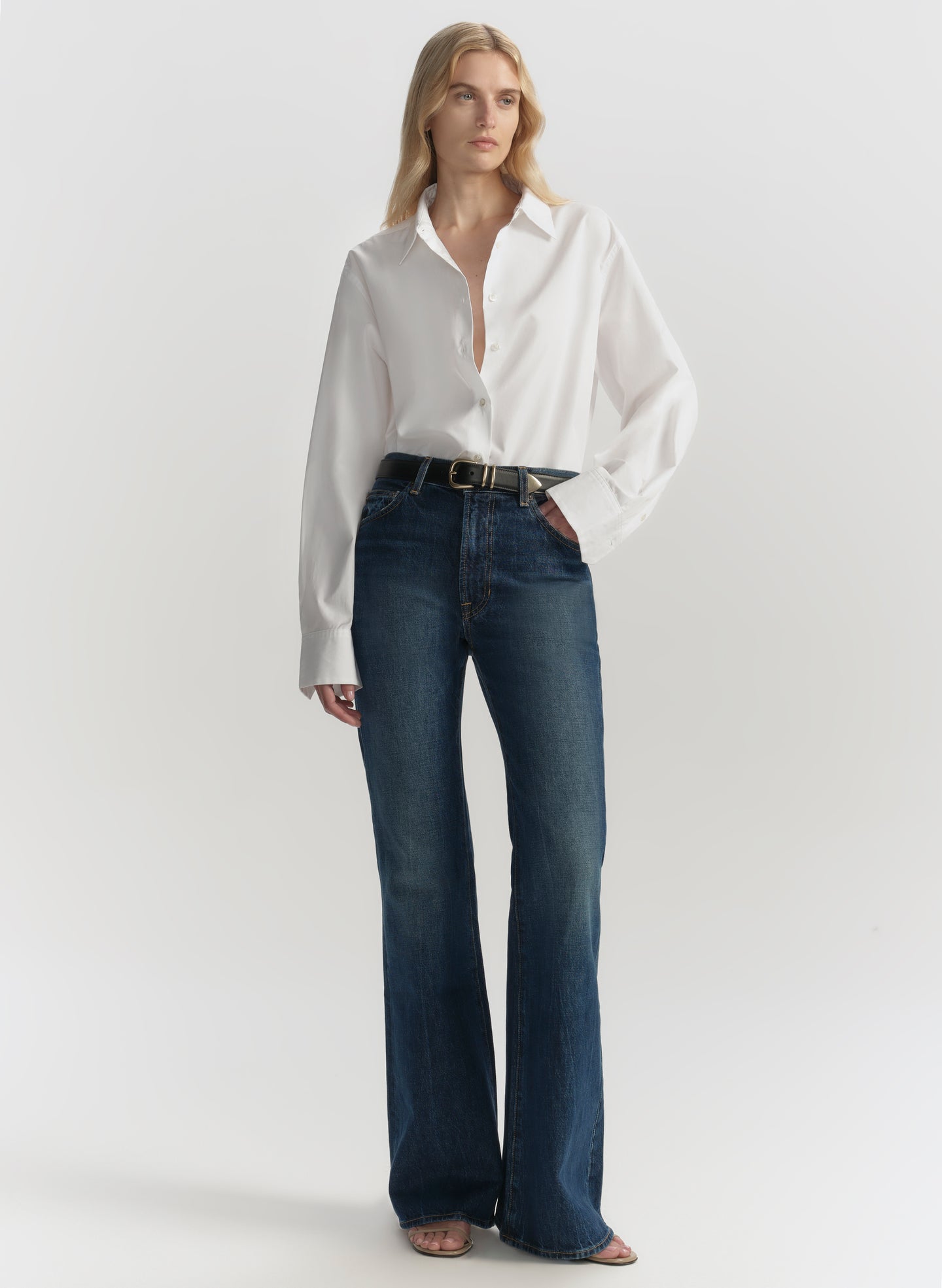 Woman wearing a white blouse and blue jeans on a plain background