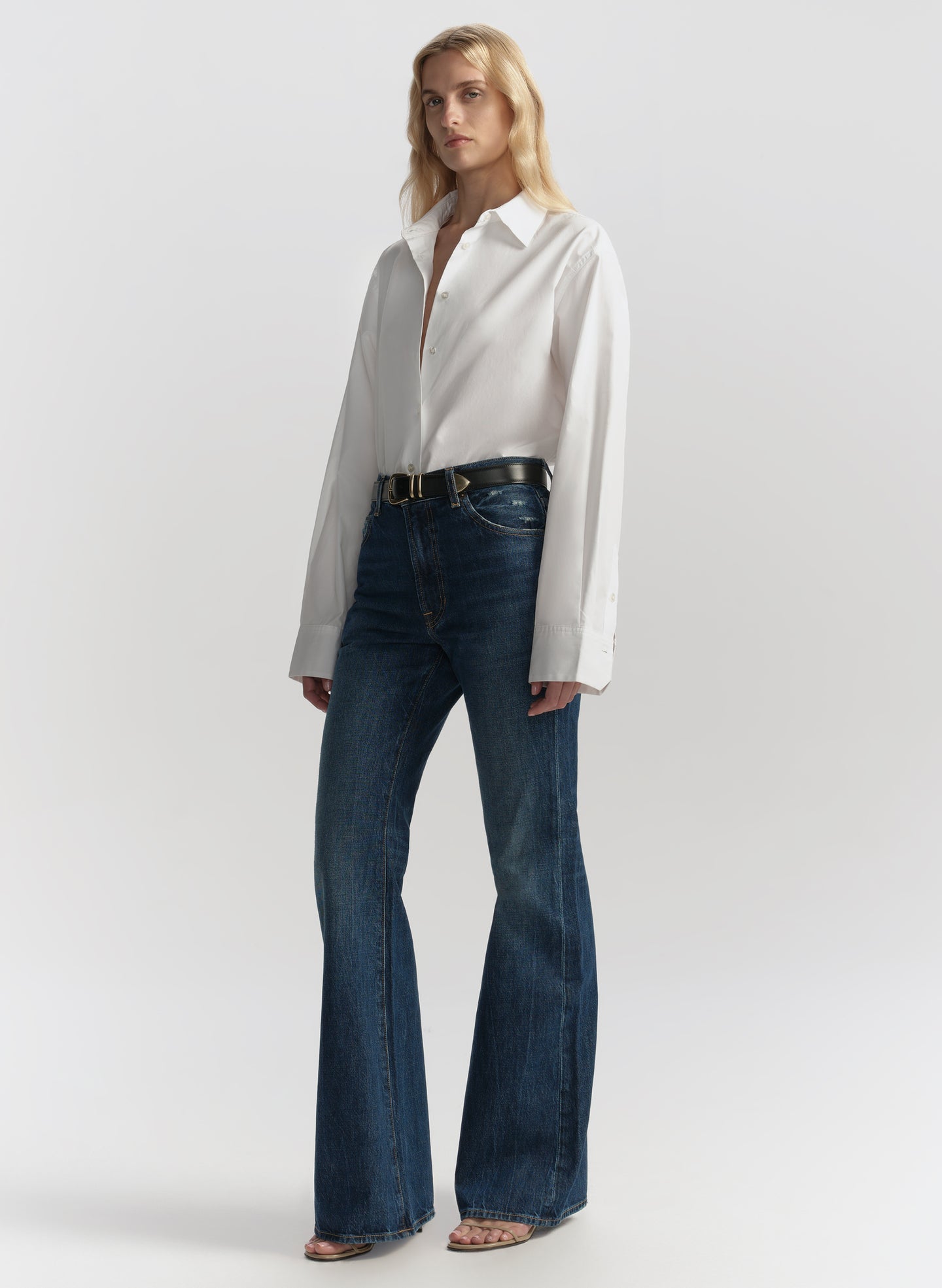 Woman wearing a white blouse and blue jeans on a plain background