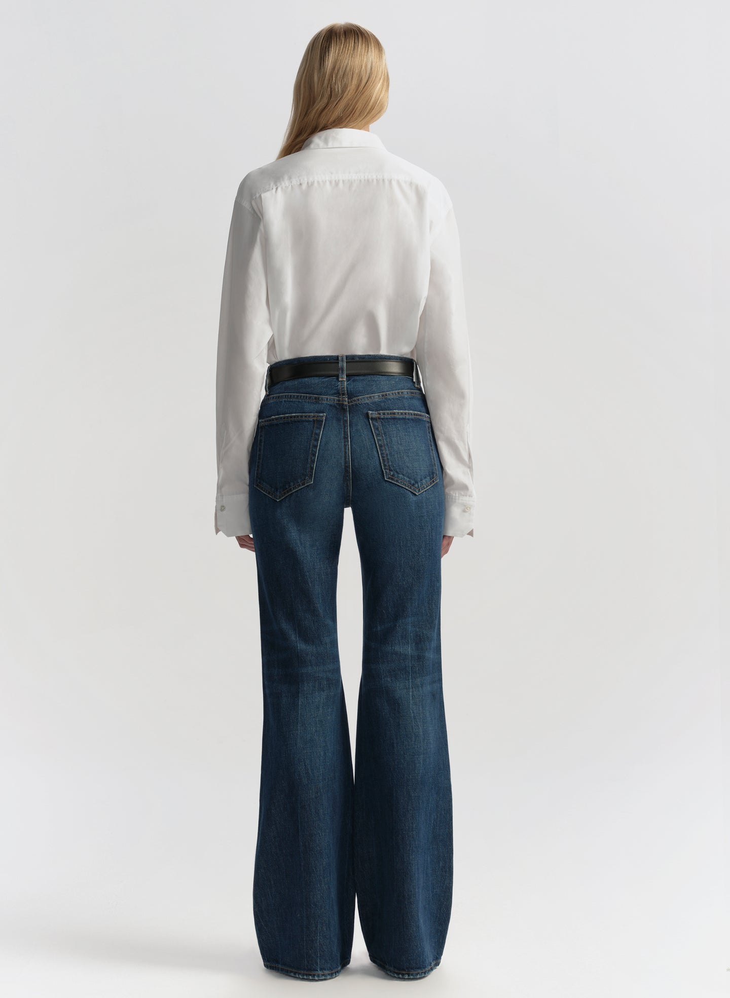 Woman wearing a white blouse and blue jeans on a plain background