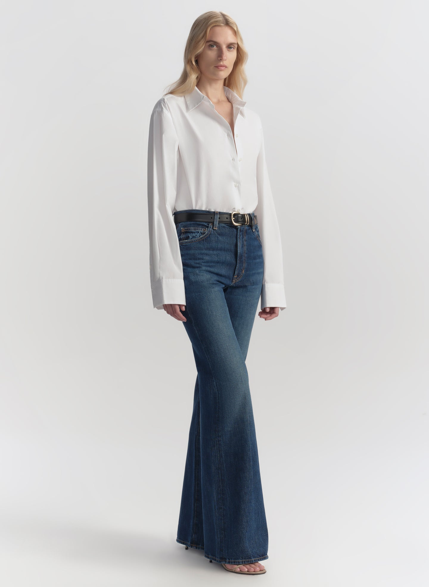 Woman wearing a white blouse and blue jeans on a plain background