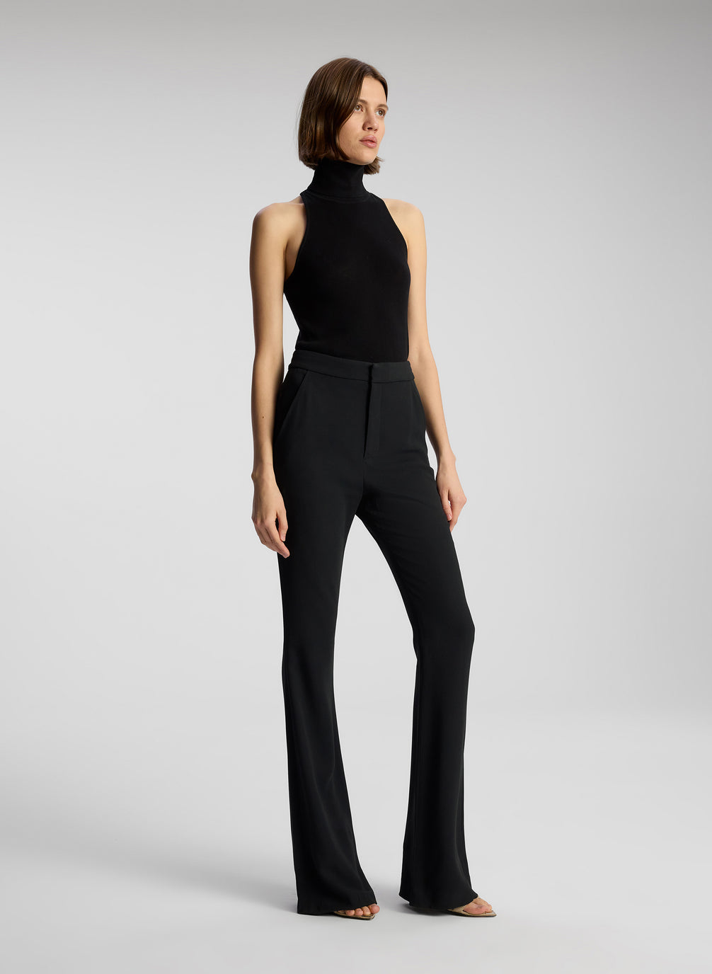 side view of woman wearing black sleeveless turtleneck and black pants