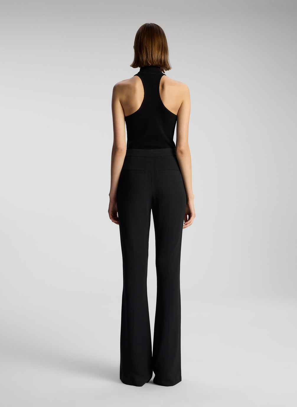 back view of woman wearing black sleeveless turtleneck and black pants