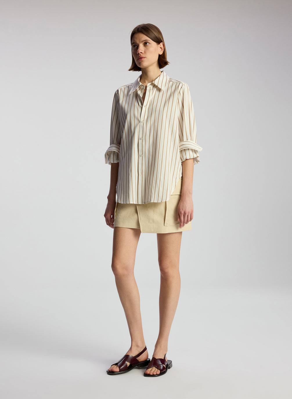 side view of woman wearing brown and white striped shirt and beige mini skirt