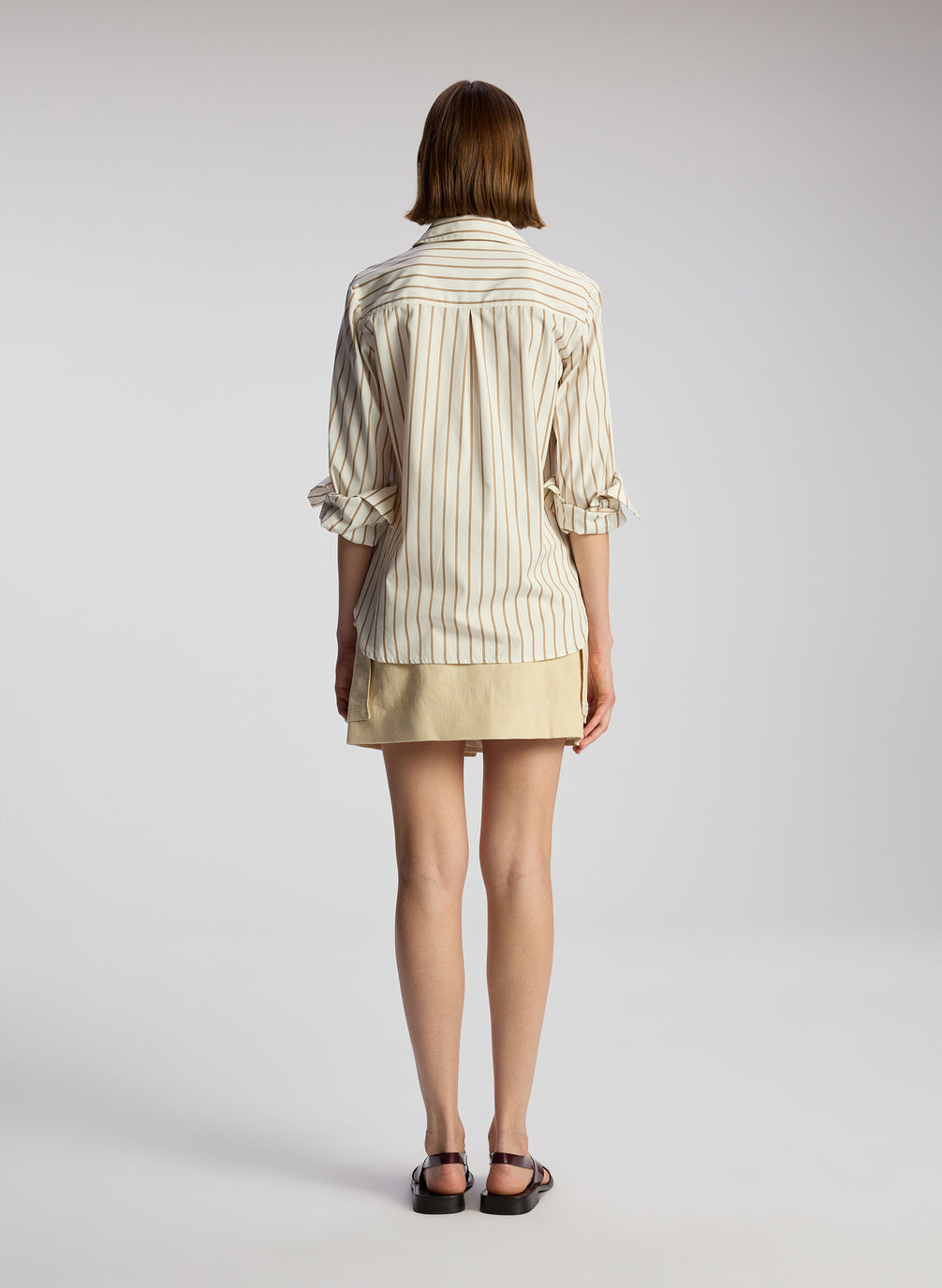 back view of woman wearing brown and white striped shirt and beige mini skirt