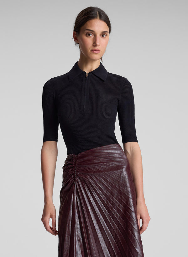 woman wearing black short sleeve collared shirt and burgundy pleated vegan leather skirt