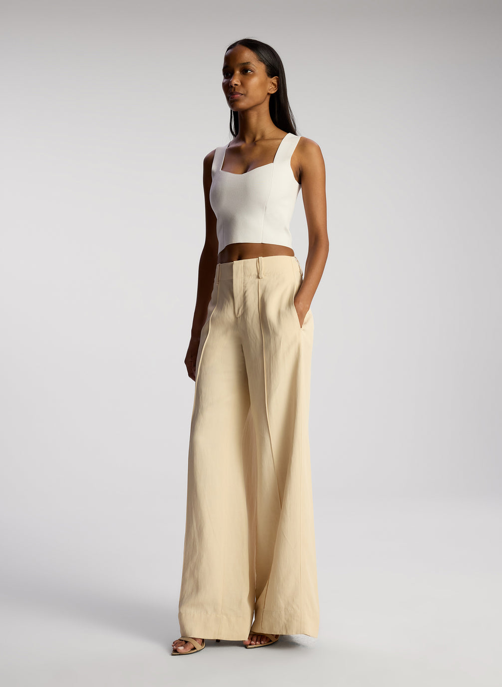 side view of view of woman wearing white compact knit tank and beige pants
