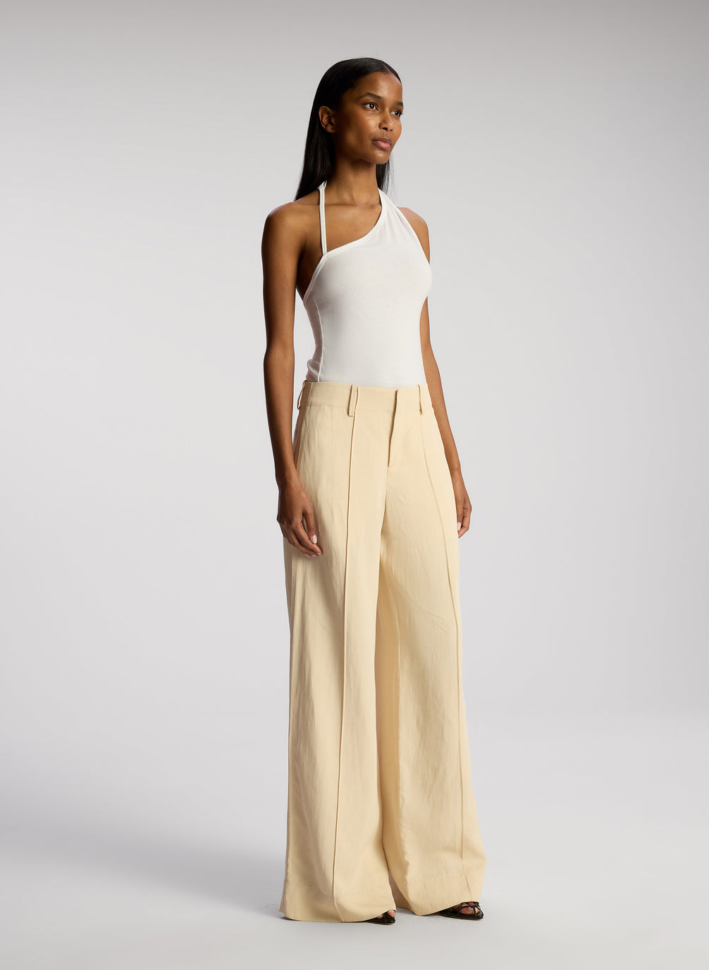 side view of woman wearing white asymmetric tank and cream wide leg pants