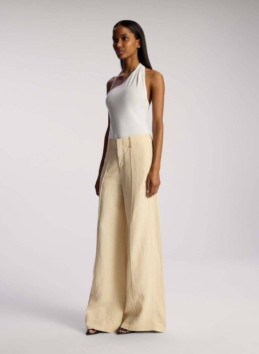 side view of woman wearing white asymmetric tank and cream wide leg pants