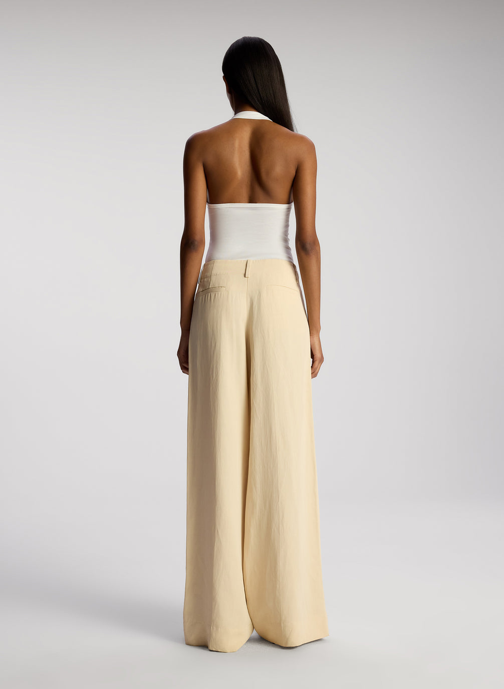 back view of woman wearing white asymmetric tank and cream wide leg pants