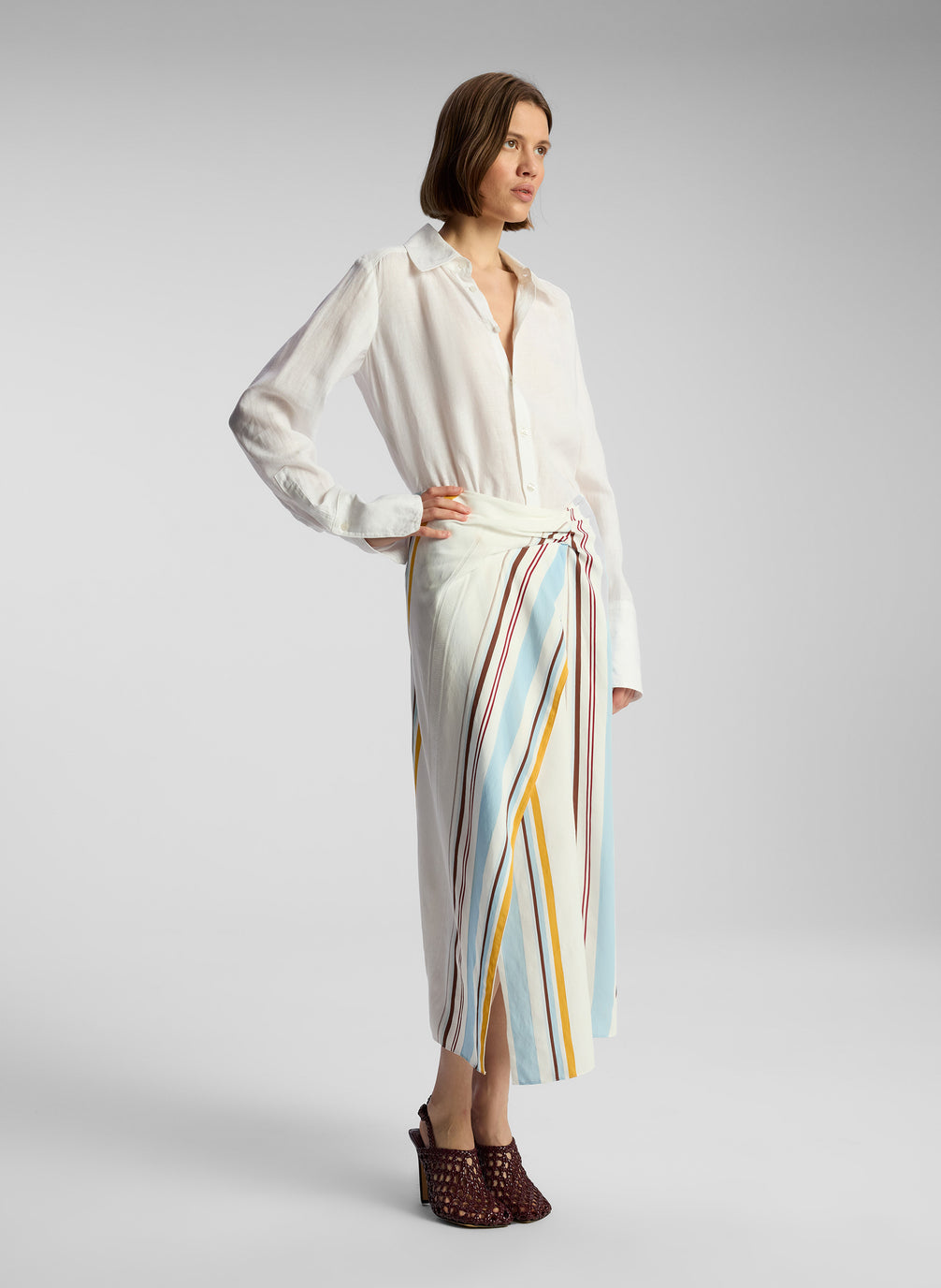 side view of woman wearing white button down shirt and multicolor striped skirt