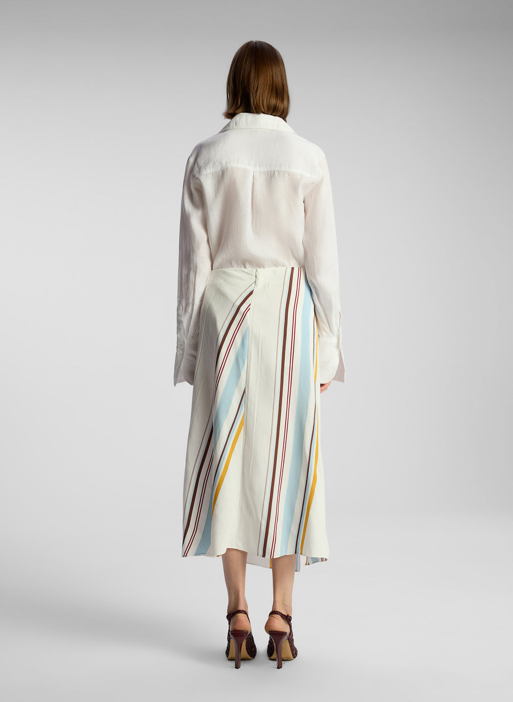 back view of woman wearing white button down shirt and multicolor striped skirt
