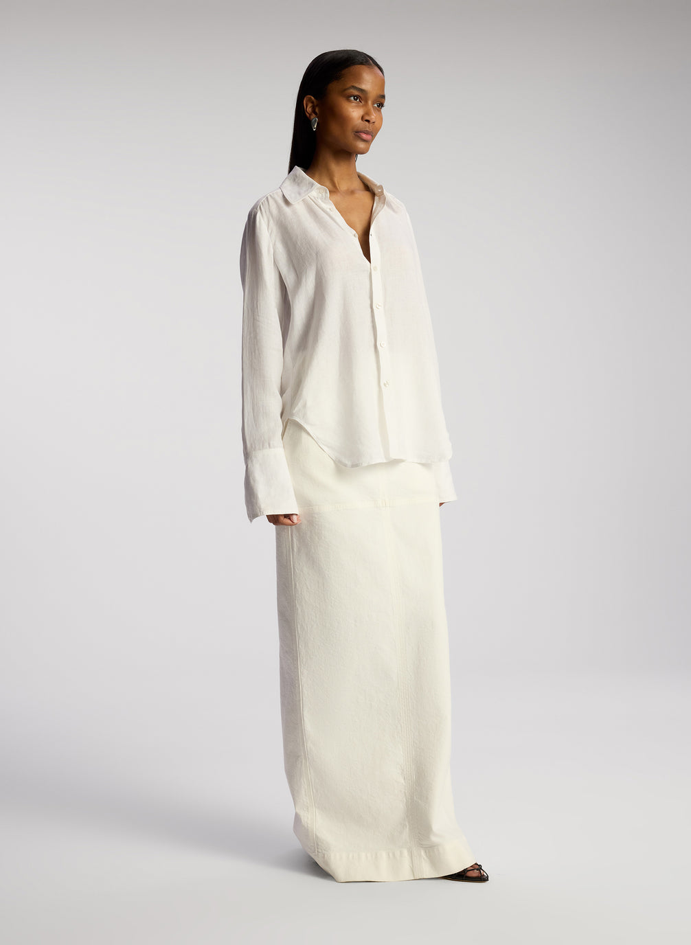 side view woman wearing white button down linen shirt and white maxi skirt