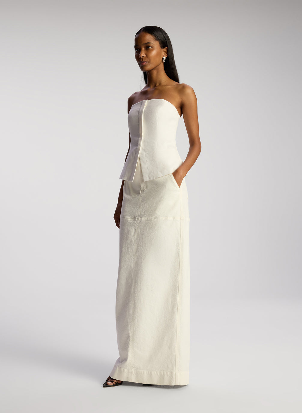 side view of woman wearing white strapless top and white maxi skirt