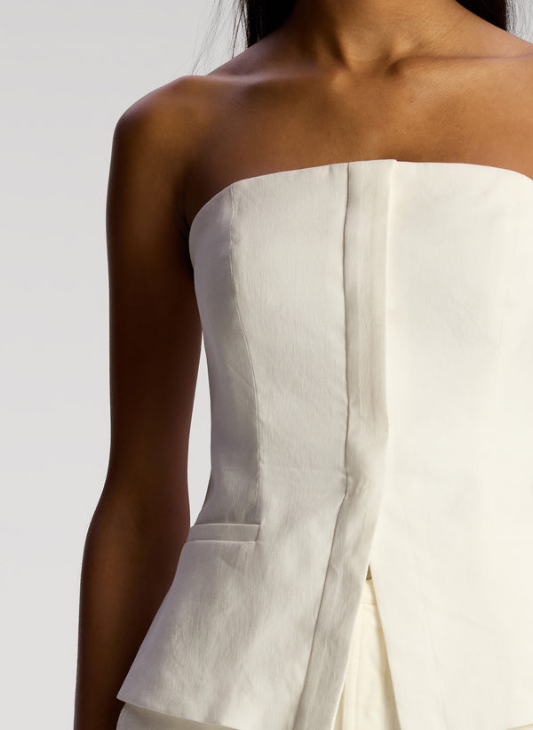 detail view of woman wearing white strapless top and white maxi skirt