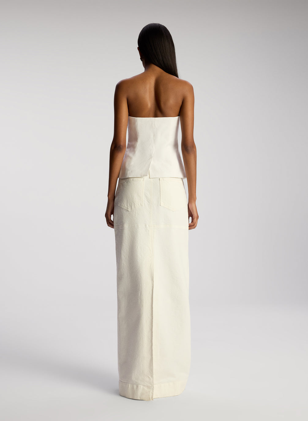 back view of woman wearing white strapless top and white maxi skirt