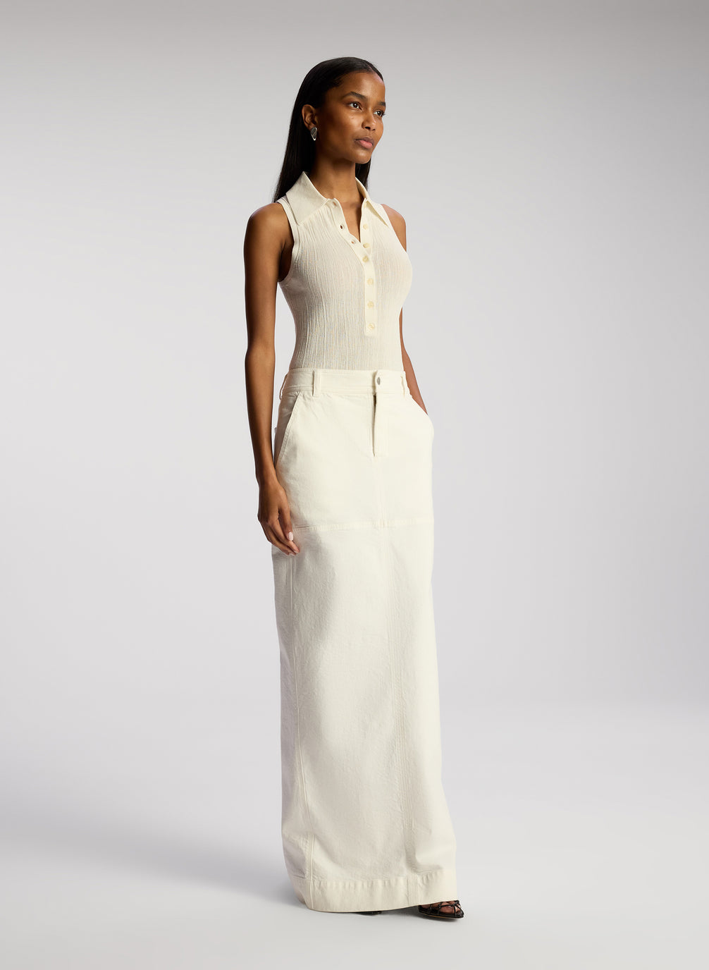 side view of woman wearing white sleeveless collared shirt and whit maxi skirt