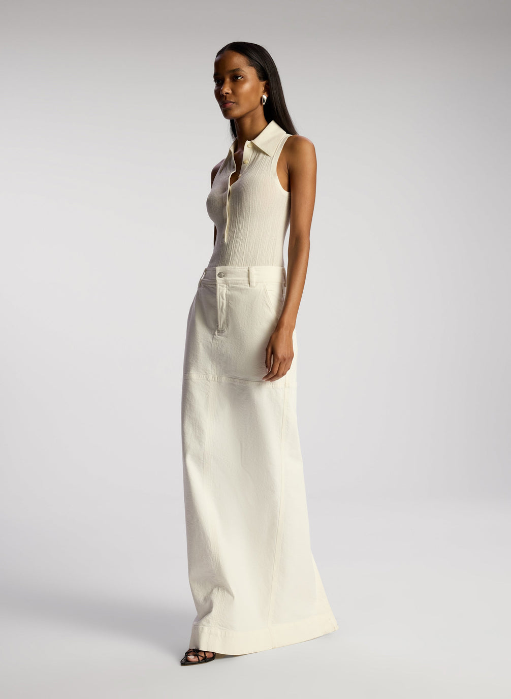 side view of woman wearing white sleeveless collared shirt and whit maxi skirt