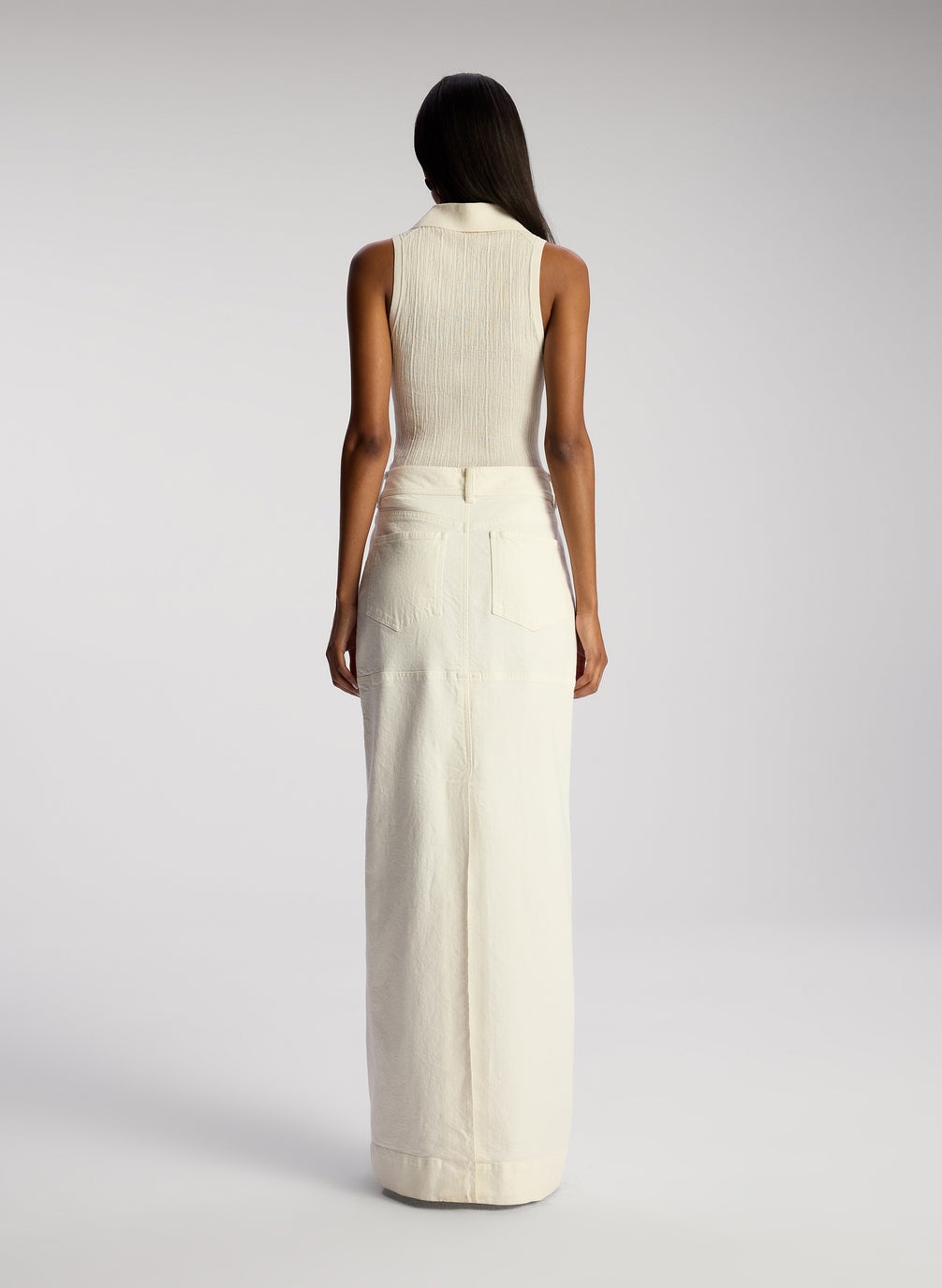 back view of woman wearing white sleeveless collared shirt and whit maxi skirt