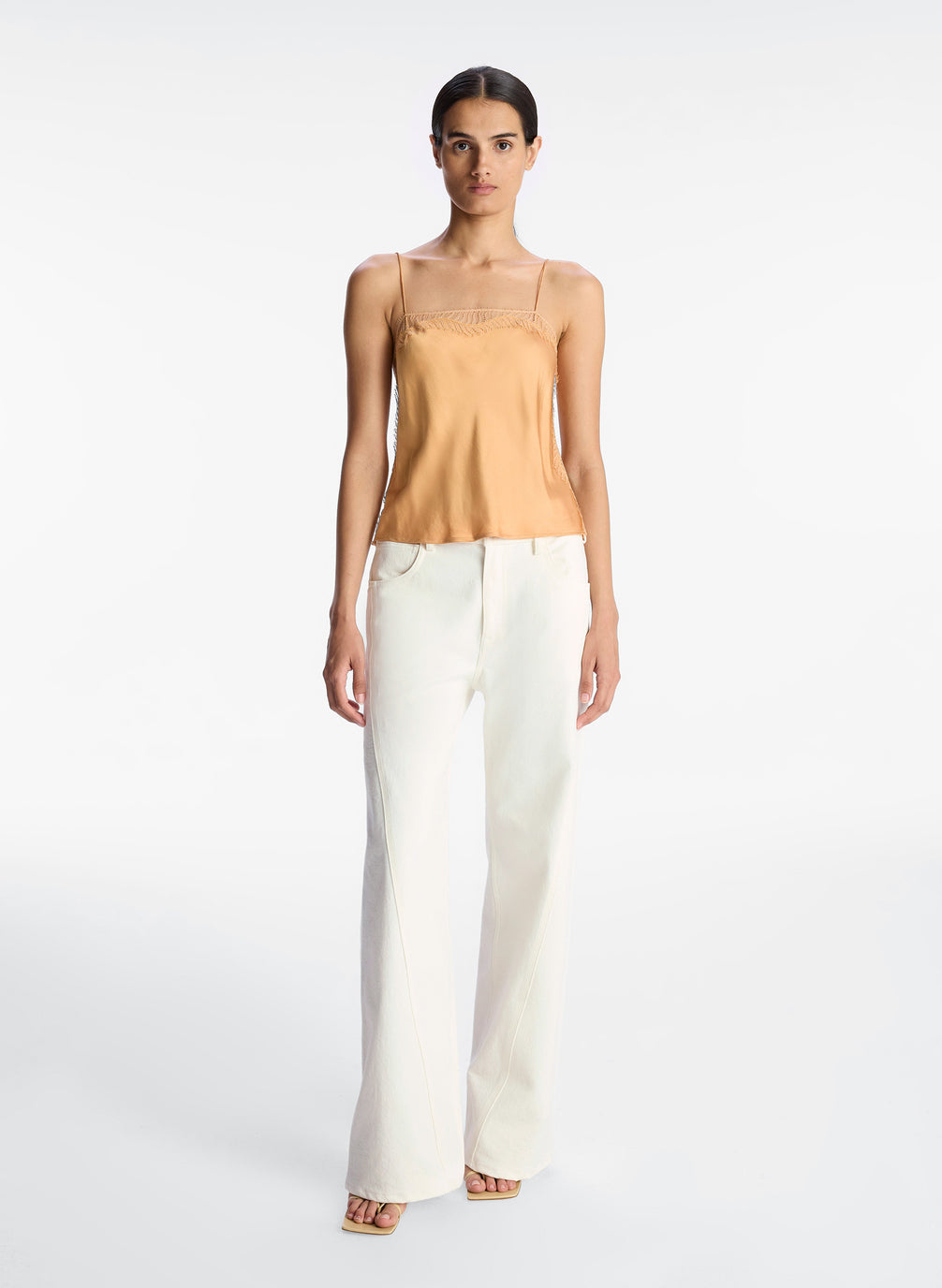 front view of woman wearing tan lace trim camisole and white pants