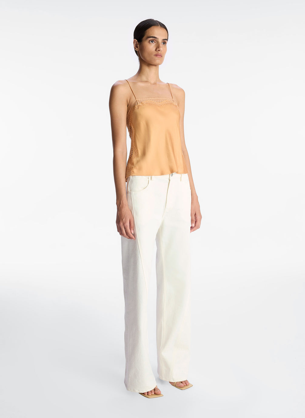 side view of woman wearing tan lace trim camisole and white pants
