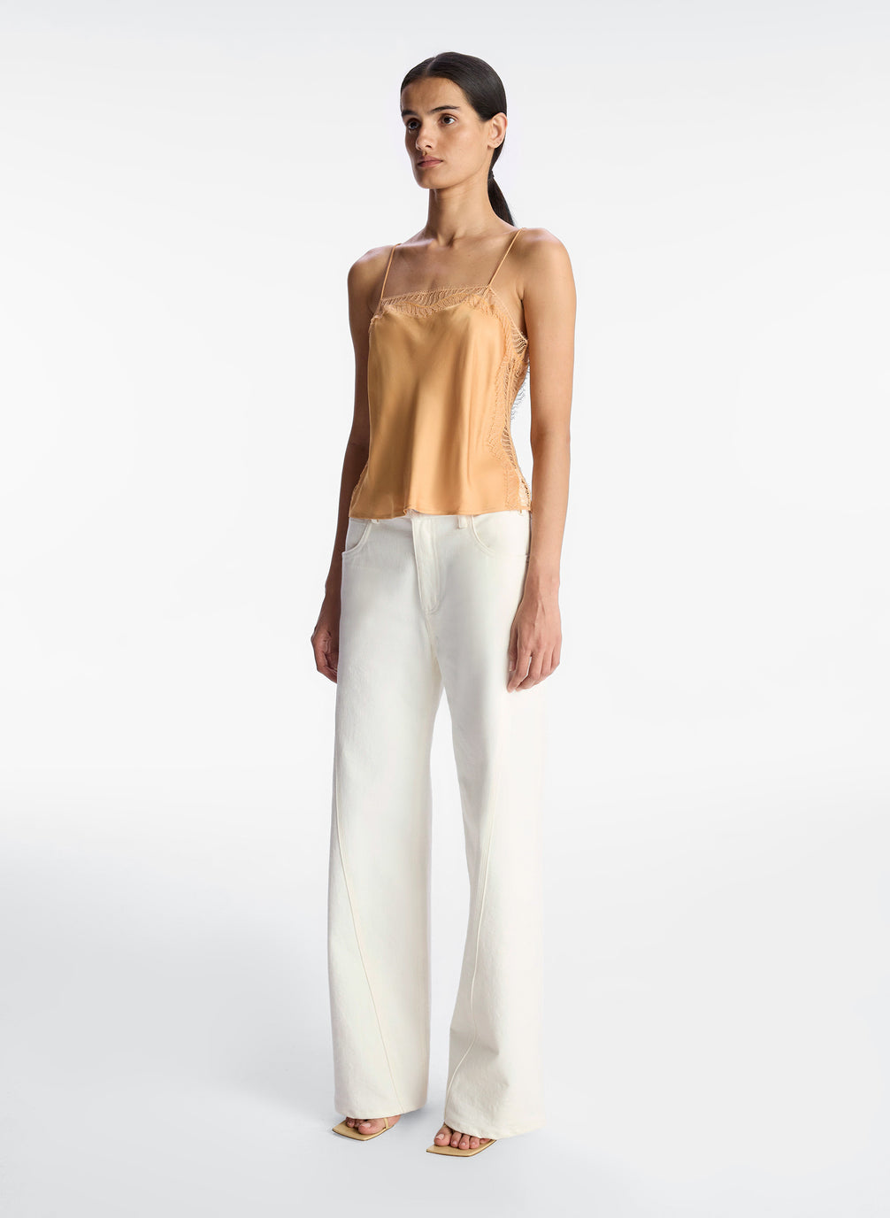 side view of woman wearing tan lace trim camisole and white pants