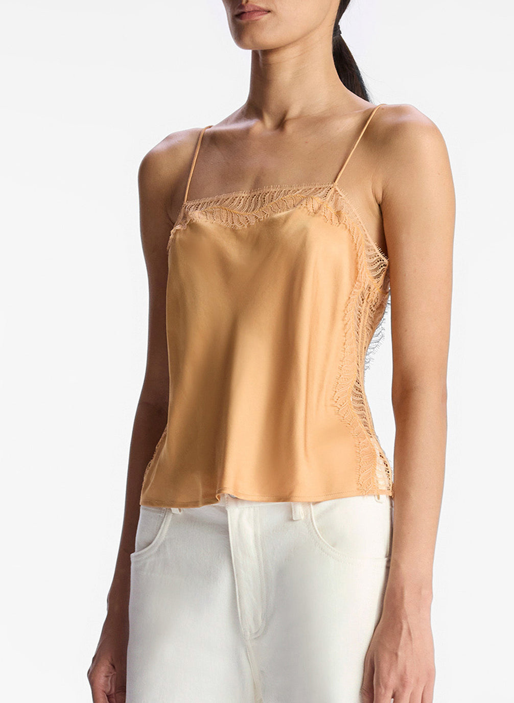 detail view of woman wearing tan lace trim camisole and white pants