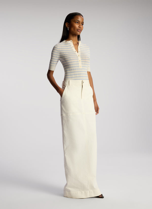 side view of woman wearing white and blue striped top and white maxi skirt