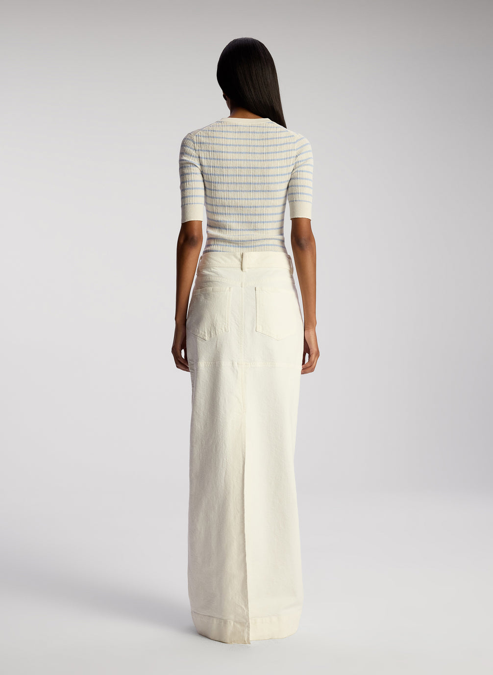 back view of woman wearing white and blue striped top and white maxi skirt