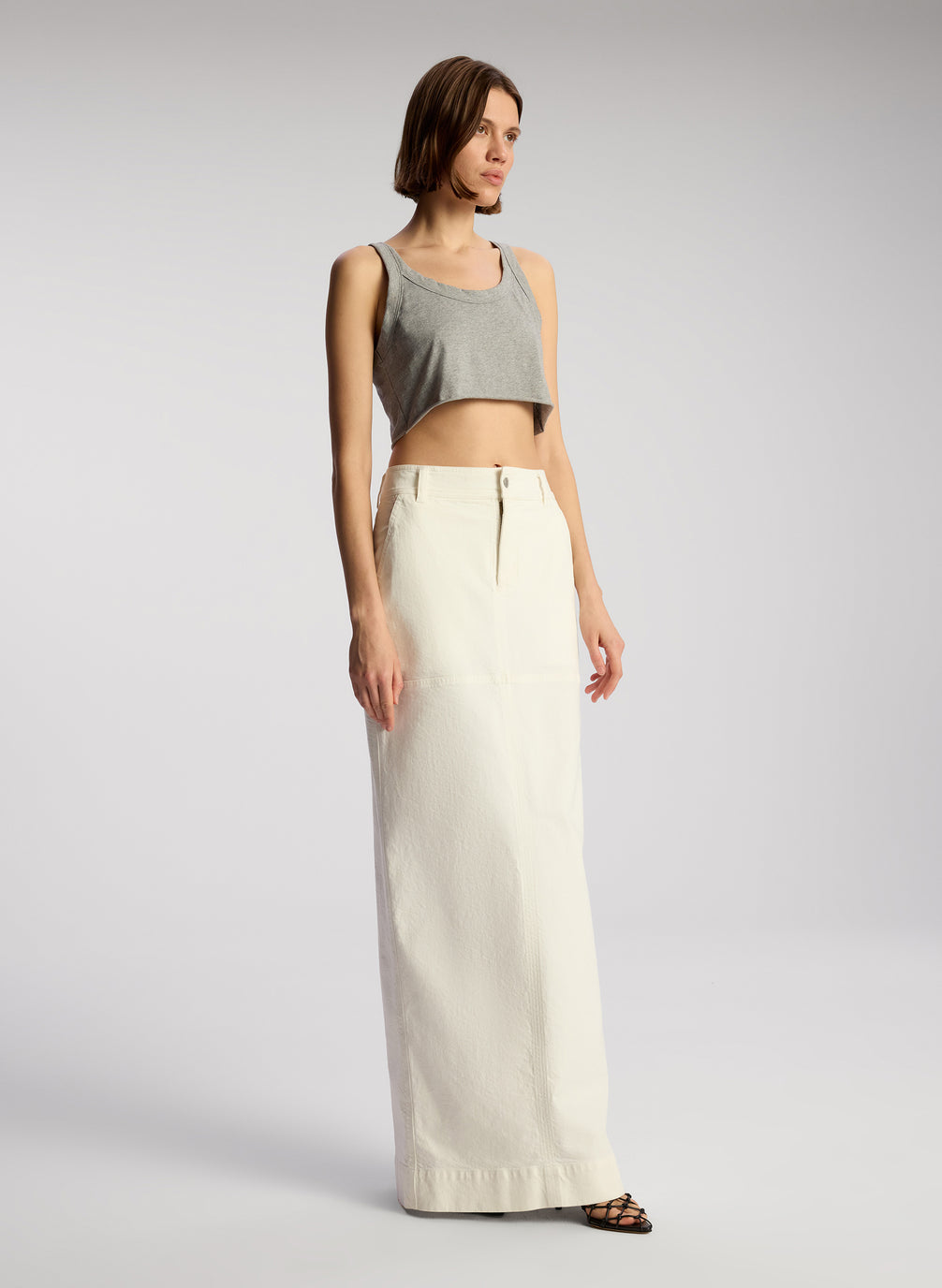 side view of woman wearing grey cropped tank and whit maxi skirt