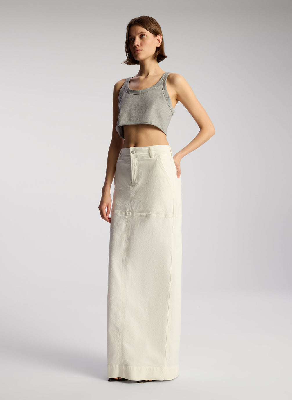 side view of woman wearing grey cropped tank and whit maxi skirt