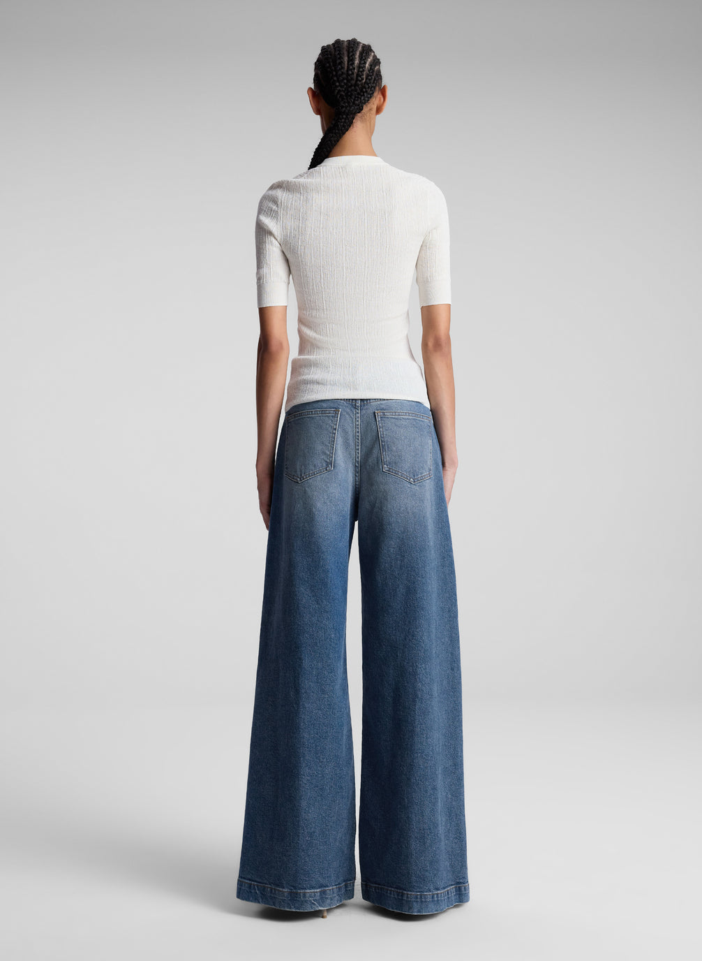 Person wearing a white top and blue jeans on a gray background