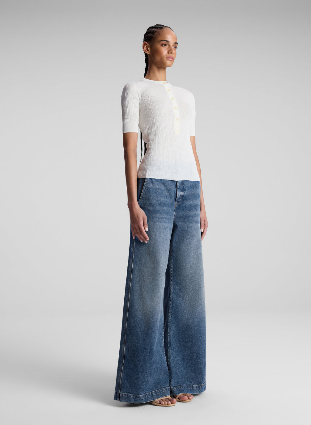 Woman wearing a white top and blue jeans on a gray background